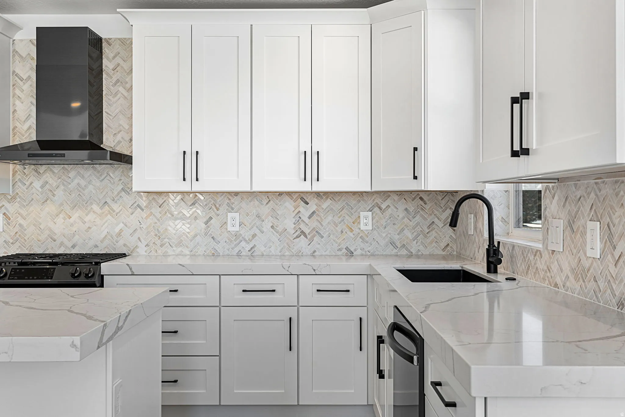Modern kitchen featuring white shaker-style cabinetry with matte black hardware, white quartz countertops, a herringbone tile backsplash in neutral tones, stainless steel appliances including a gas cooktop and undermount sink with matte black faucet, and