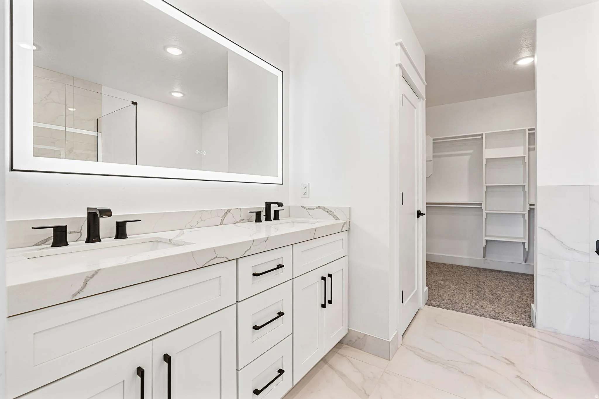 Dual vanity with stone-finish countertop, matte black fixtures, and an illuminated mirror