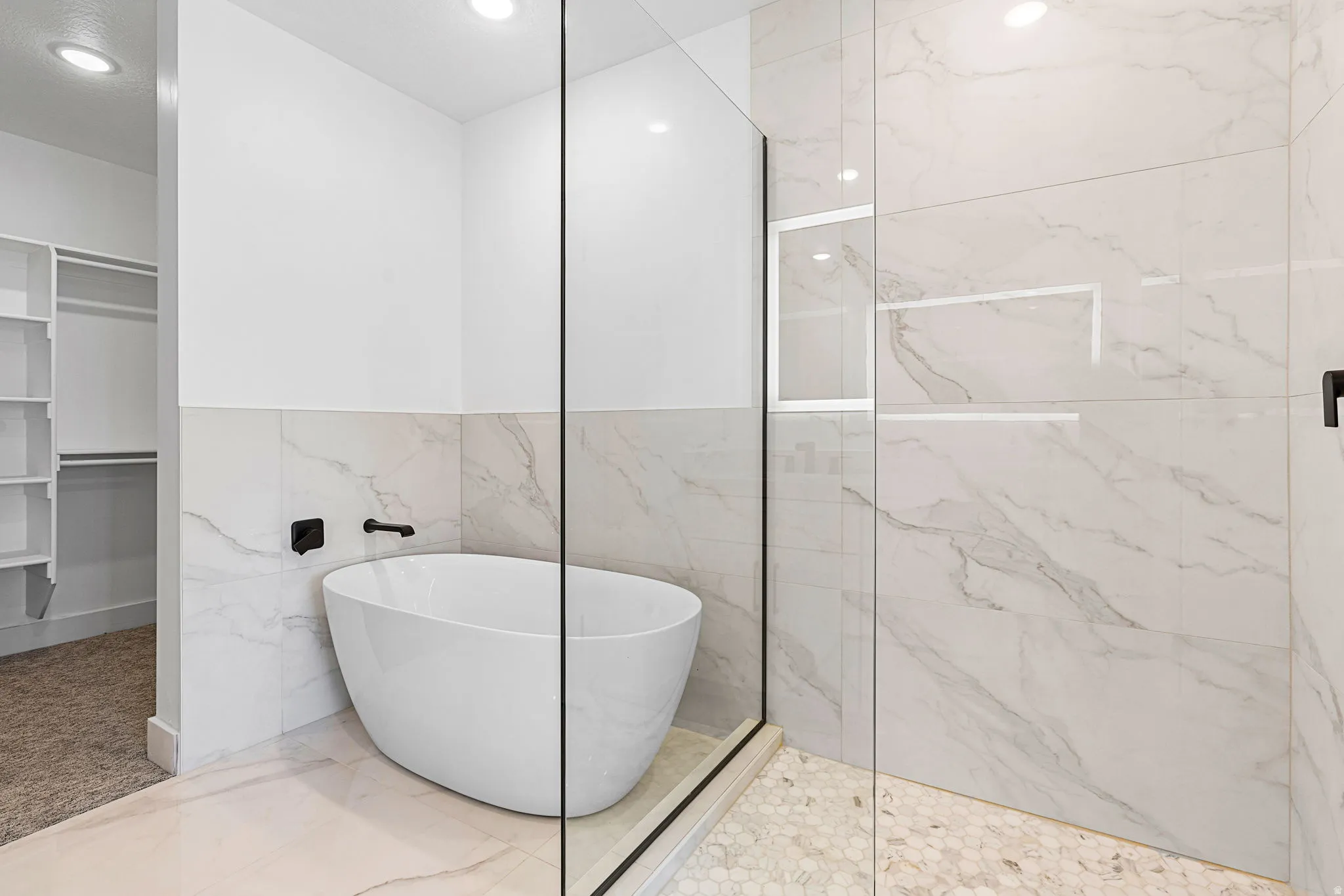 Freestanding soaking tub with matte black fixtures, glass-enclosed shower with a recessed shelf, and large-format tile walls