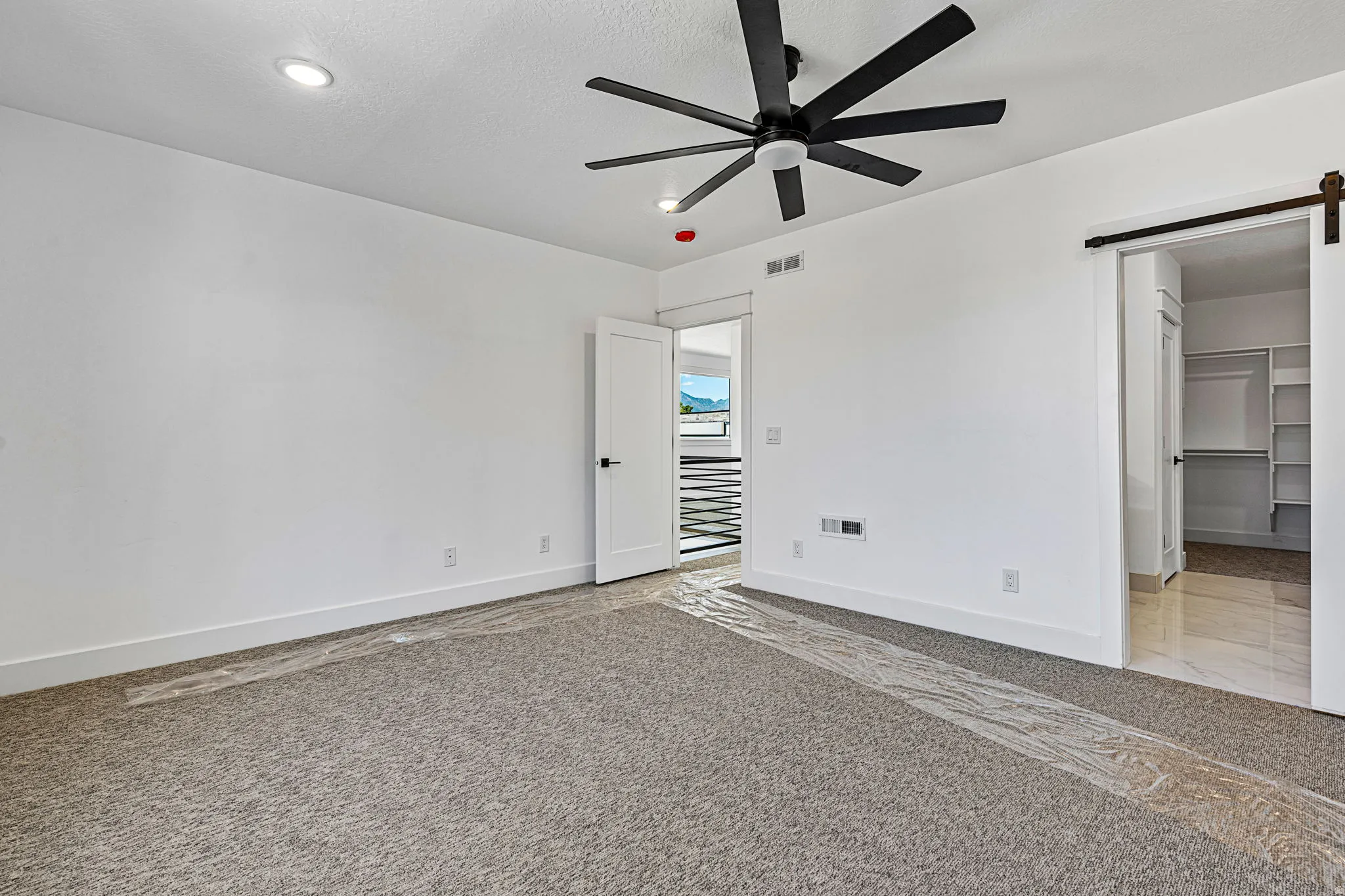 Recessed ceiling lighting, modern black ceiling fan, white paneled doors, sliding barn door hardware, and an open closet with built-in shelving