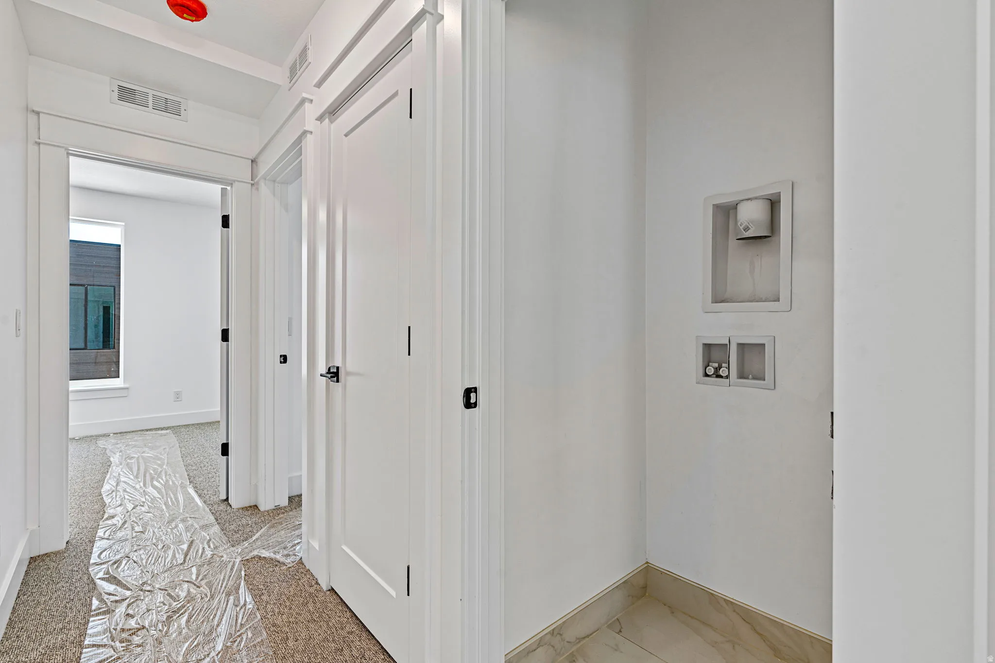 Dedicated laundry area with stone tile flooring, adjacent to a carpeted hallway with a flush-mount ceiling light
