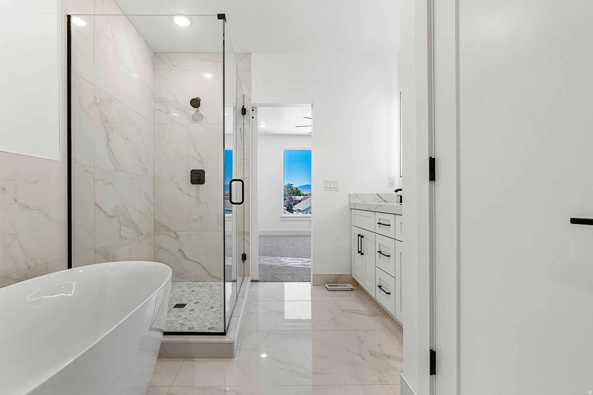 Freestanding soaking tub, frameless glass shower enclosure with tile surround, dual vanity with stone countertop, tile flooring, and matte black fixtures