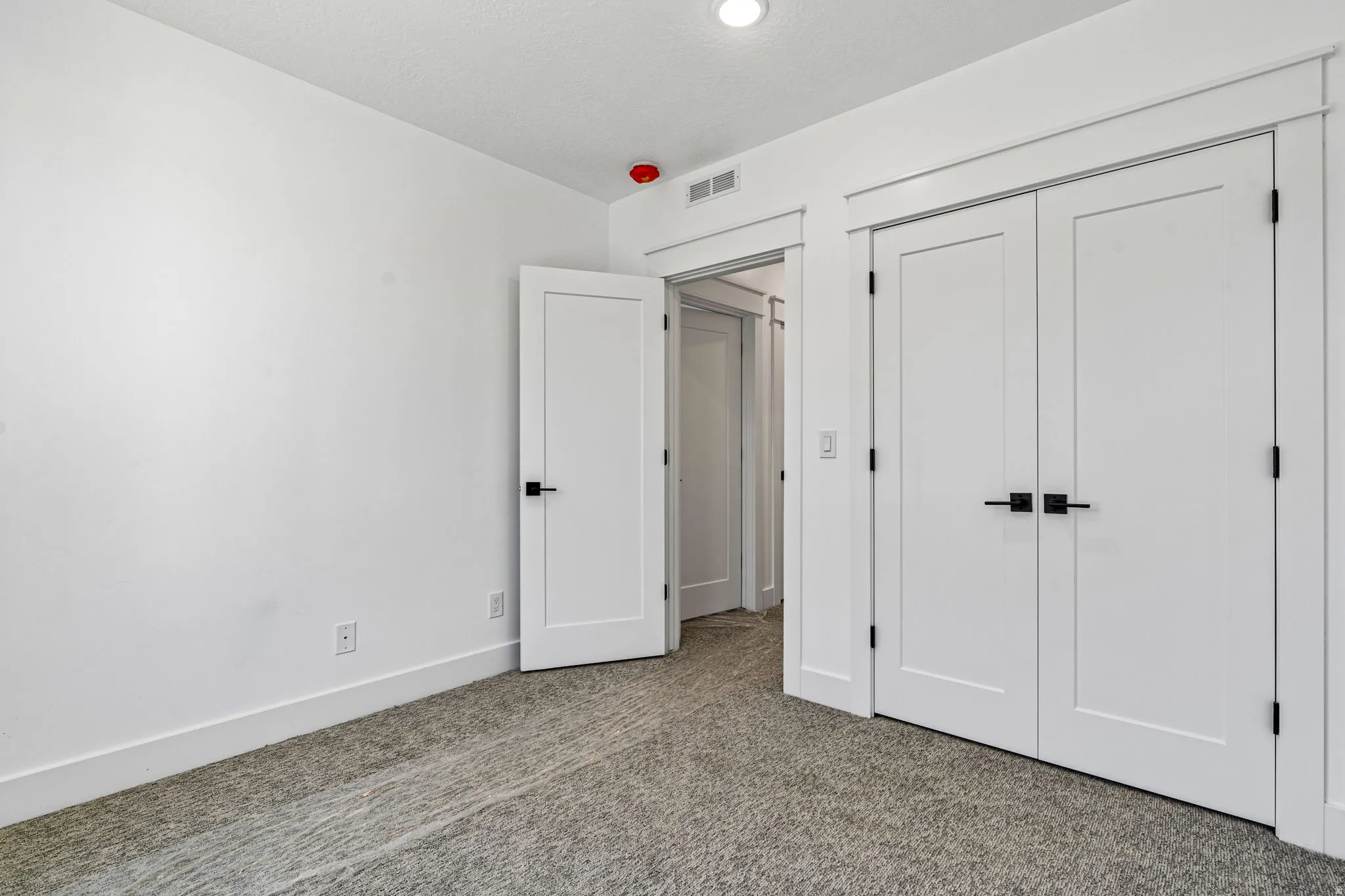 Neutral-toned carpeting, white walls, white doors with matte black hardware, and recessed ceiling lighting