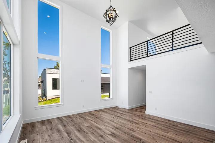 Two-story living area featuring tall windows, a loft with a horizontal metal railing, wood-finish flooring, and a decorative ceiling light fixture