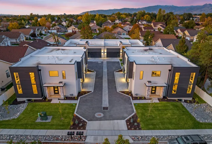 Modern architectural design with contrasting dark and light exterior panels, expansive flat rooflines, integrated two-car garages, and a paved central driveway