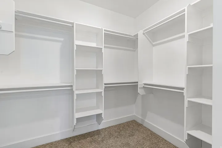 White shelving units, multiple hanging rods, built-in shelving, carpet flooring