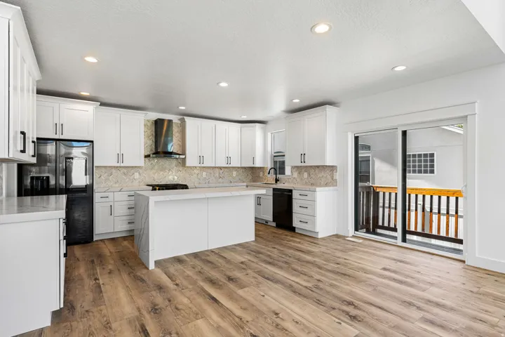 Kitchen featuring white cabinetry, a large kitchen island, stainless steel appliances, wood-finish flooring, and a sliding glass door