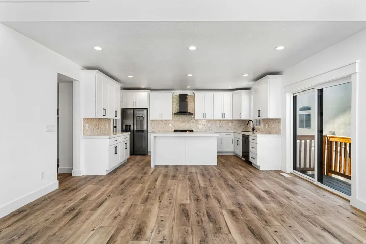 Open-concept kitchen featuring white cabinetry, a central island, stainless steel appliances, and a tile backsplash