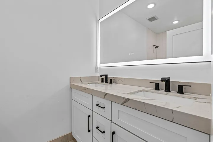 Dual basin vanity with white cabinetry, matte black hardware, and integrated sinks