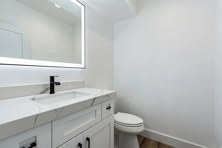 White vanity with shaker-style cabinetry, matte black hardware, integrated sink, and quartz countertop