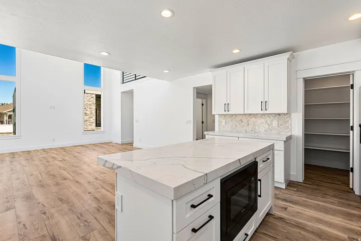 Kitchen island with a light-toned countertop, white cabinetry with black hardware, and wood-finish flooring