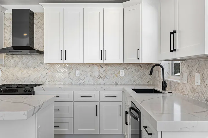 Modern kitchen featuring white shaker-style cabinetry with matte black hardware, white quartz countertops, a herringbone tile backsplash in neutral tones, stainless steel appliances including a gas cooktop and undermount sink with matte black faucet, and