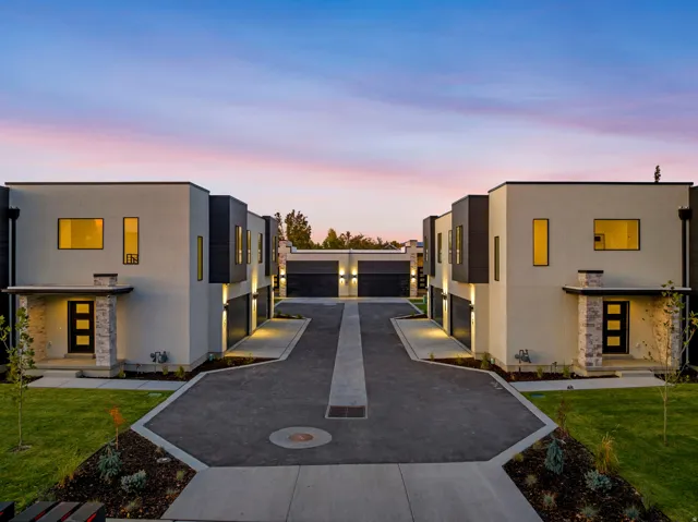 Modern exterior architecture with clean lines, contrasting dark and light facade elements, integrated exterior lighting, attached garages, and a paved central driveway