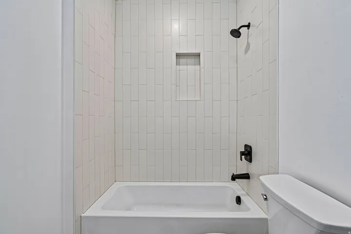 Bathtub with vertical subway tile surround, matte black shower fixtures, and a recessed shower niche