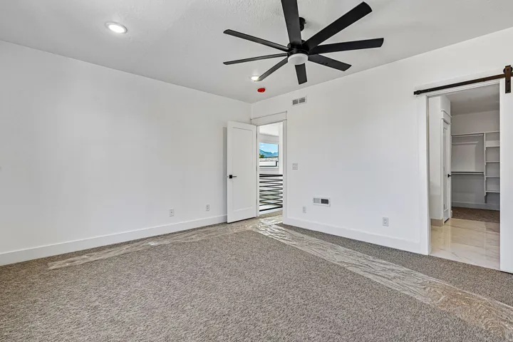 Recessed ceiling lighting, modern black ceiling fan, white paneled doors, sliding barn door hardware, and an open closet with built-in shelving
