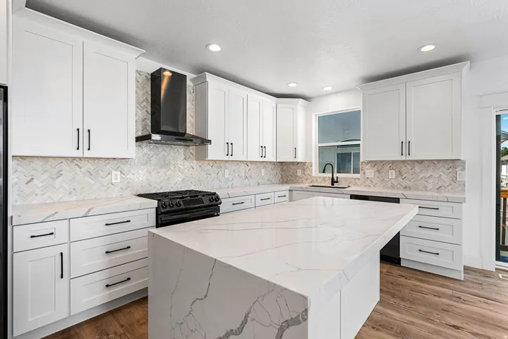 Kitchen featuring a large island with a waterfall countertop, white shaker cabinetry, stainless steel appliances, and wood-finish flooring