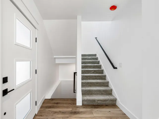 Entryway featuring a contemporary white door with integrated glass panels, matte black hardware, wood-finish flooring, and a carpeted staircase with a black handrail