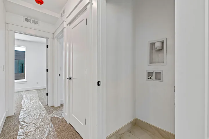 Dedicated laundry area with stone tile flooring, adjacent to a carpeted hallway with a flush-mount ceiling light