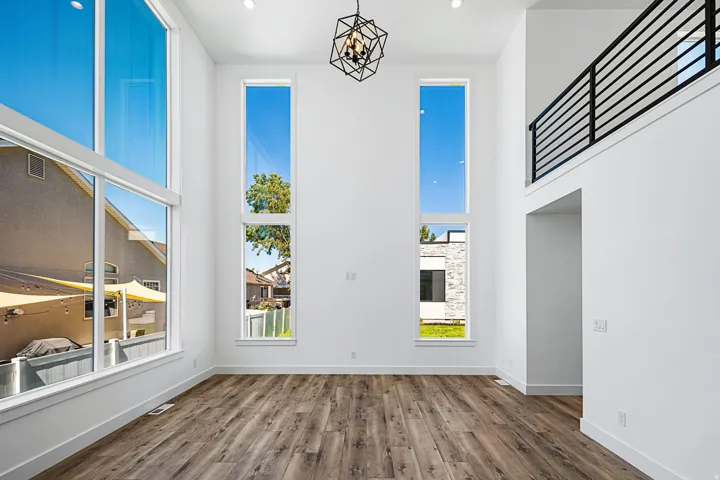 Expansive double-height ceilings, contemporary black metal railing, large floor-to-ceiling windows, wood-finish flooring, and a modern geometric light fixture