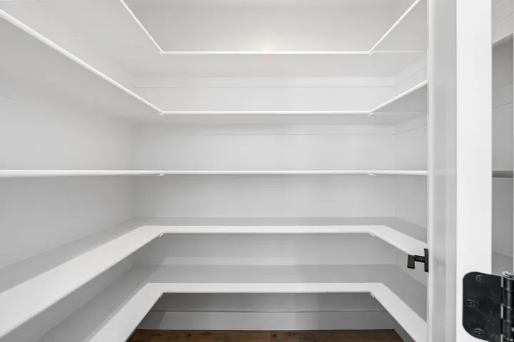 Spacious pantry featuring white built-in shelving, white walls, and wood-finish flooring