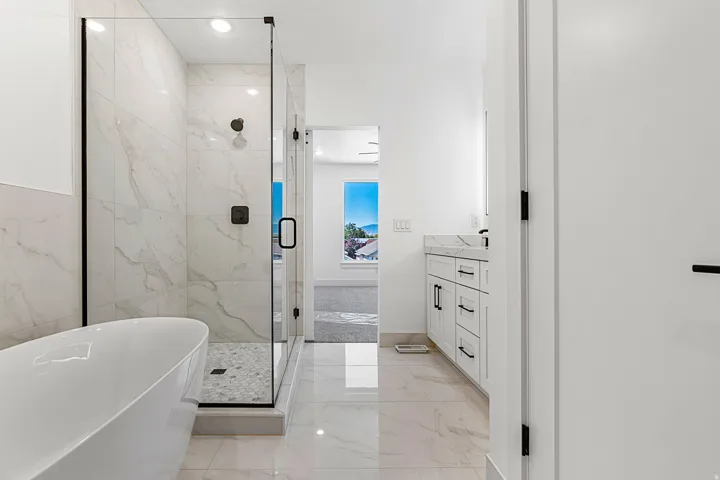Freestanding soaking tub, frameless glass shower enclosure with tile surround, dual vanity with stone countertop, tile flooring, and matte black fixtures