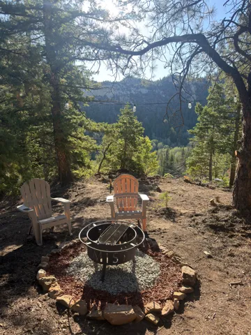 Outdoor gathering area with a decorative fire pit, natural stone border, and string lighting