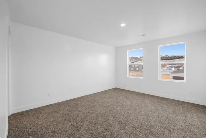 Neutral wall paint, recessed lighting, two windows, and dark carpet flooring