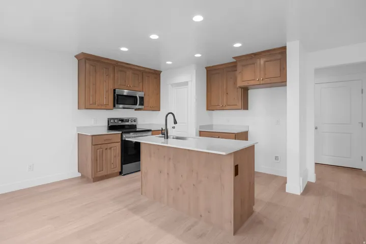 Kitchen featuring light wood-finish flooring, recessed lighting, wood cabinetry, stone countertops, and a kitchen island with an integrated sink and matte black faucet