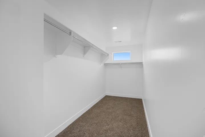 Spacious walk-in closet featuring white walls, a horizontal window, and recessed lighting