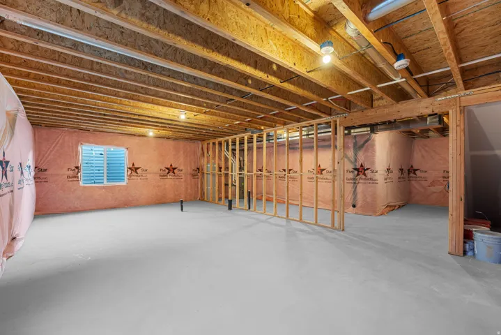 Unfinished lower level featuring exposed wood joists, framed walls, a window, and concrete flooring