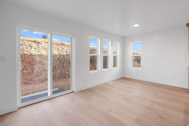 Expansive room with wood-finish flooring, white walls, multiple windows, and a sliding glass door