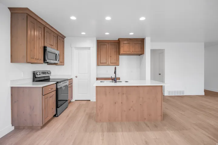 Kitchen featuring wood cabinetry, white countertops, stainless steel appliances, and a central island with an integrated sink