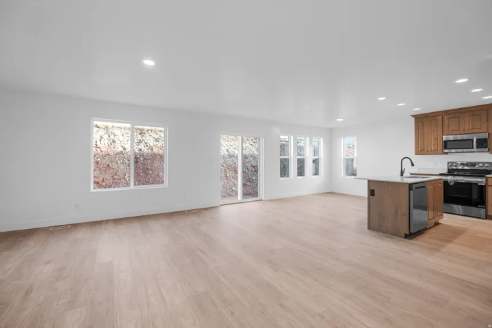 Open-concept living area featuring wood-finish flooring, recessed lighting, white walls, kitchen island with sink, and stainless steel appliances