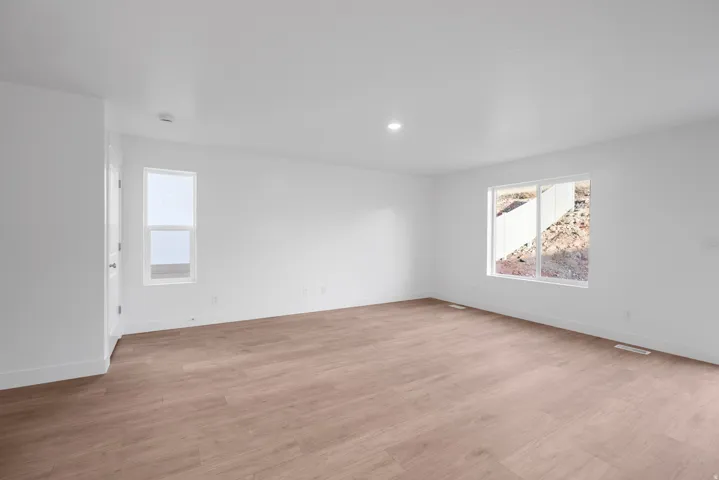 Spacious room with wood-finish flooring, white walls, recessed lighting, and large windows