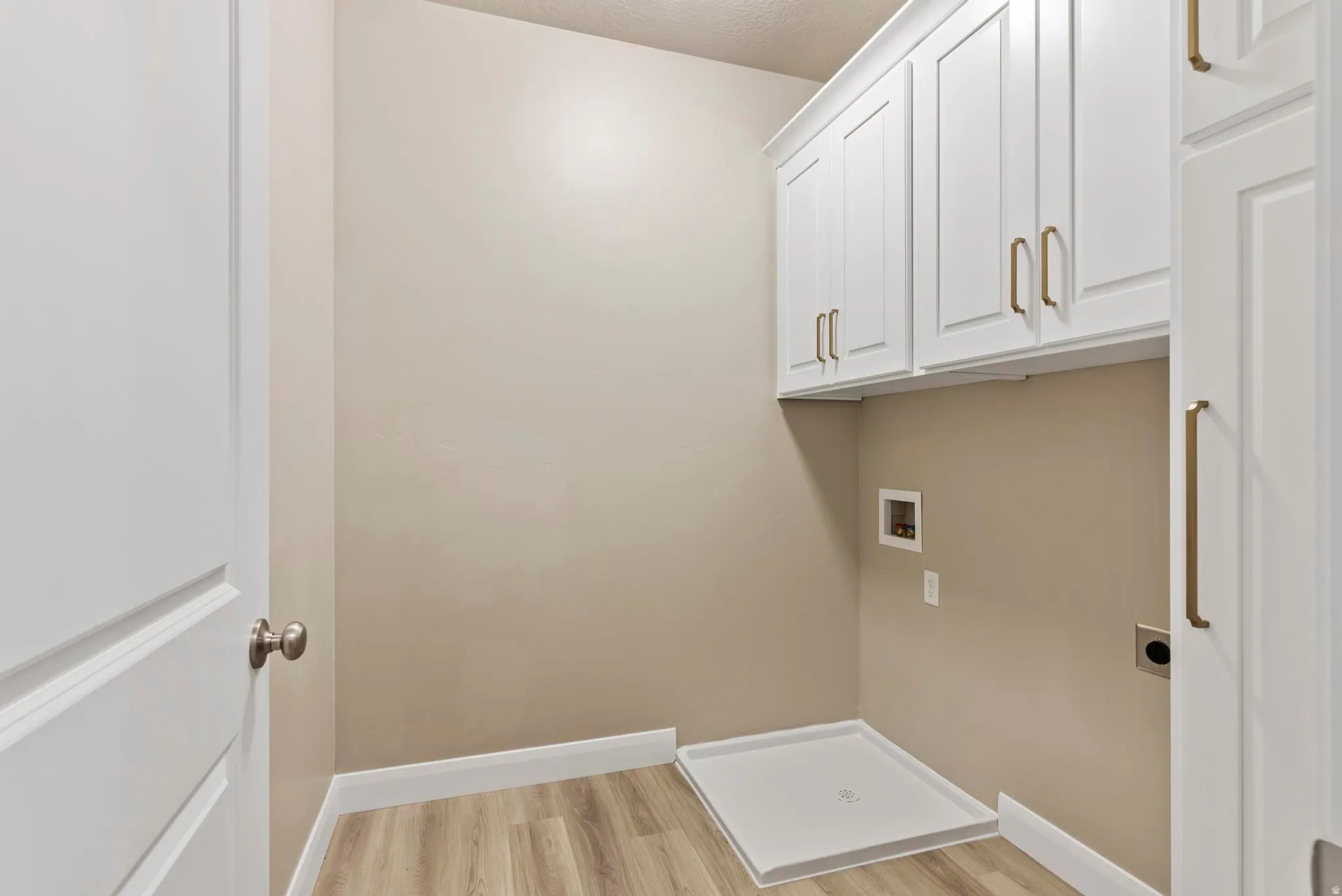White shaker-style cabinetry with gold-tone hardware, wood-finish flooring, and light neutral wall paint