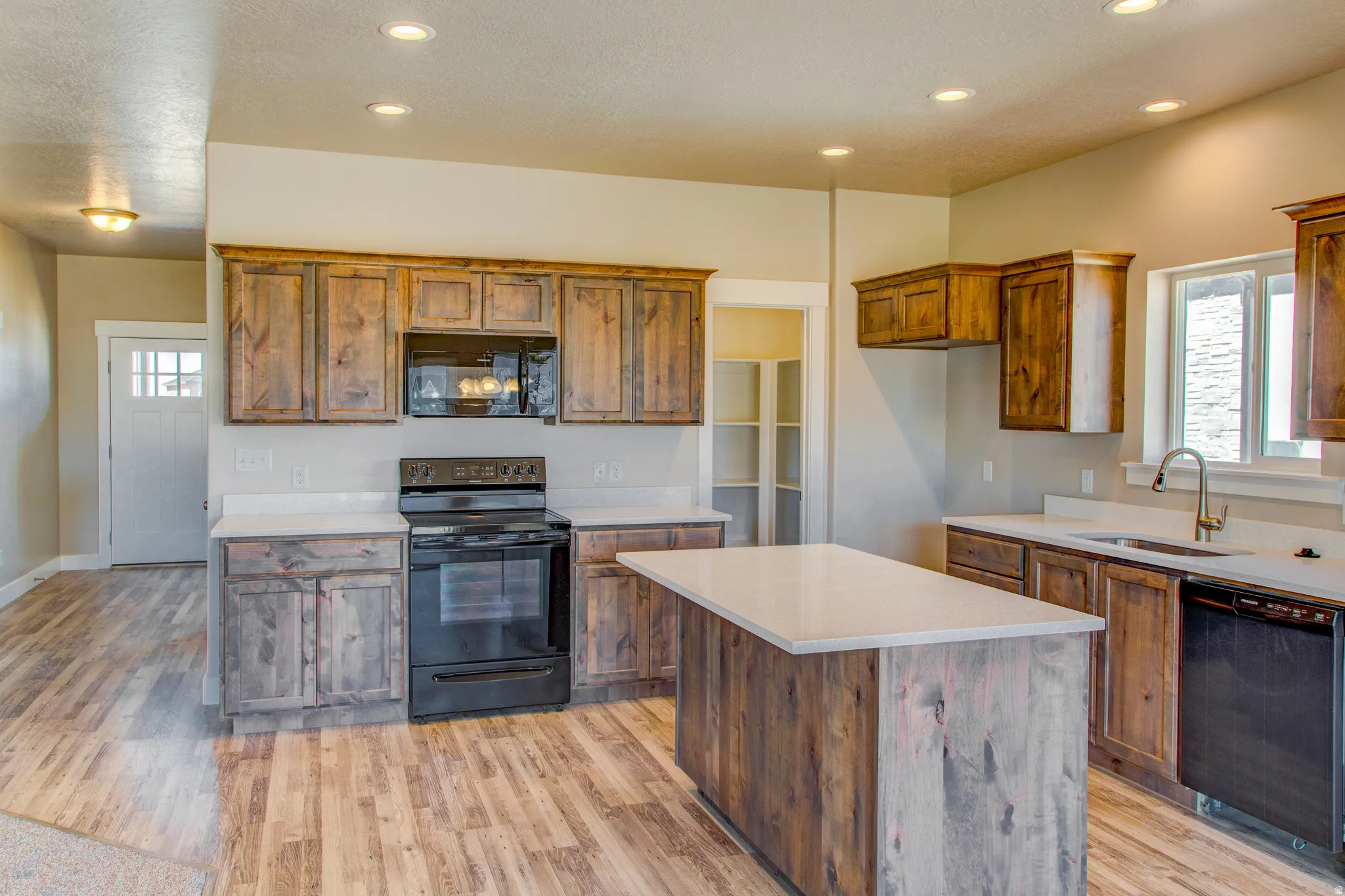 Kitchen featuring wood-finish cabinetry, white countertops, built-in microwave, black range, and wood-finish flooring
