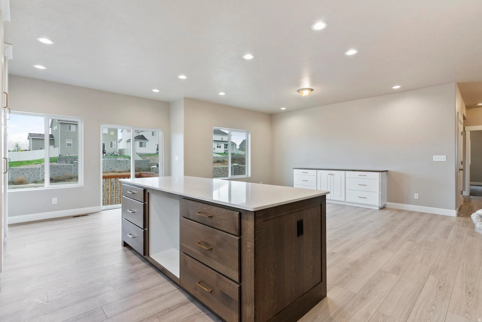 Spacious interior featuring wood-finish flooring, a large kitchen island with integrated storage, built-in white cabinetry with a dark countertop, recessed lighting, and multiple windows