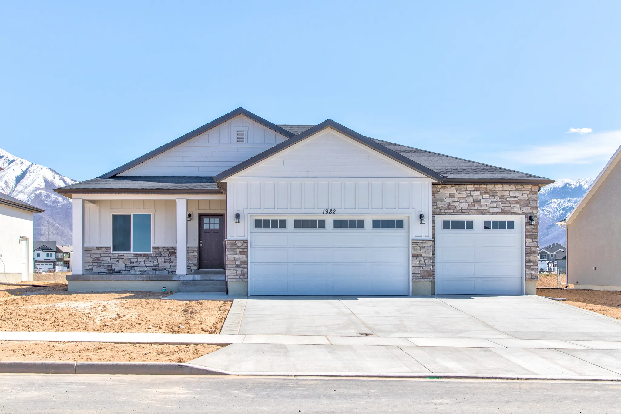 Contemporary single-story residence with stone and siding exterior, covered porch entry, and a three-car garage