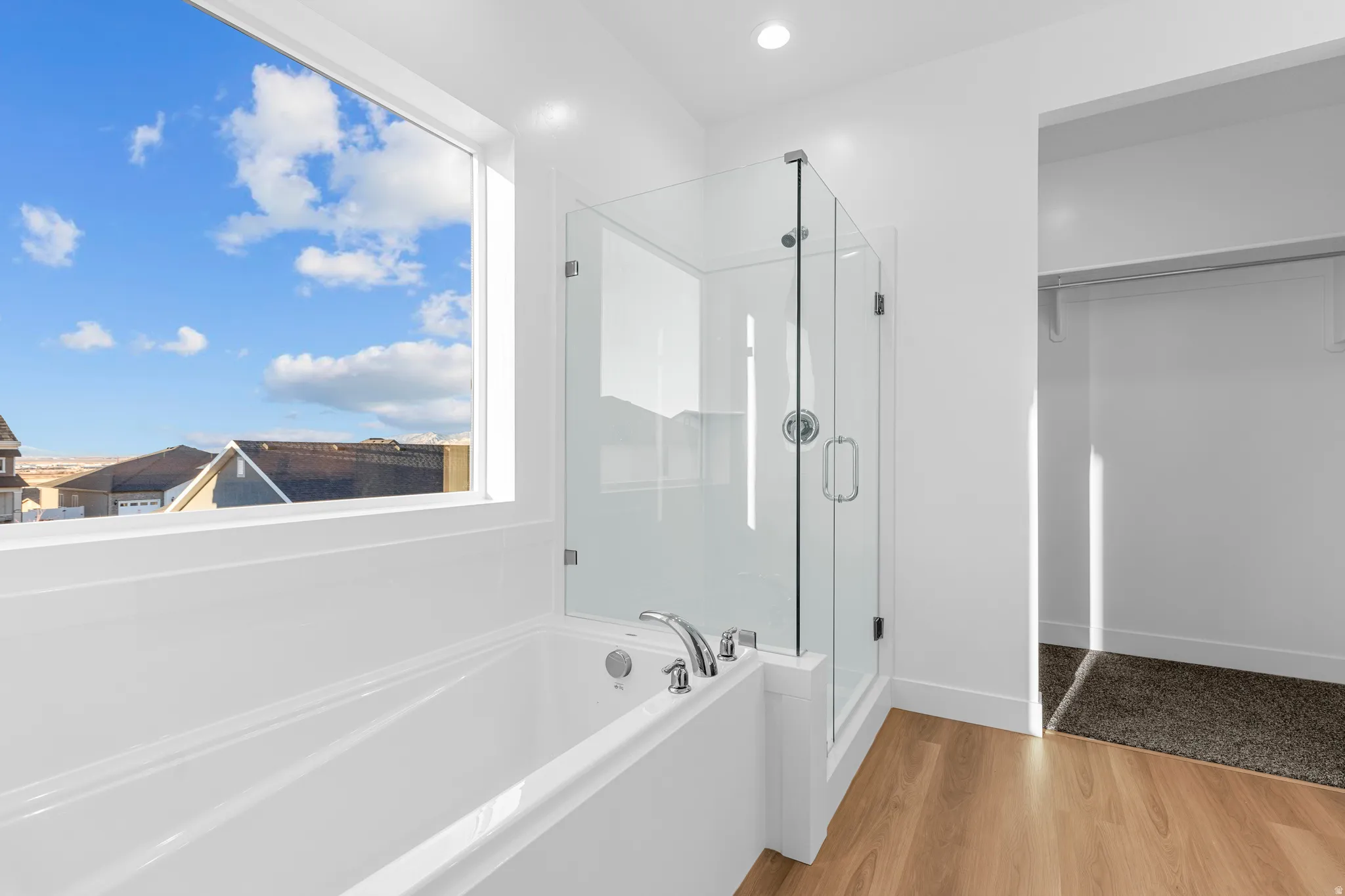 Soaking tub with a large picture window, glass-enclosed shower, wood-finish flooring, and recessed lighting