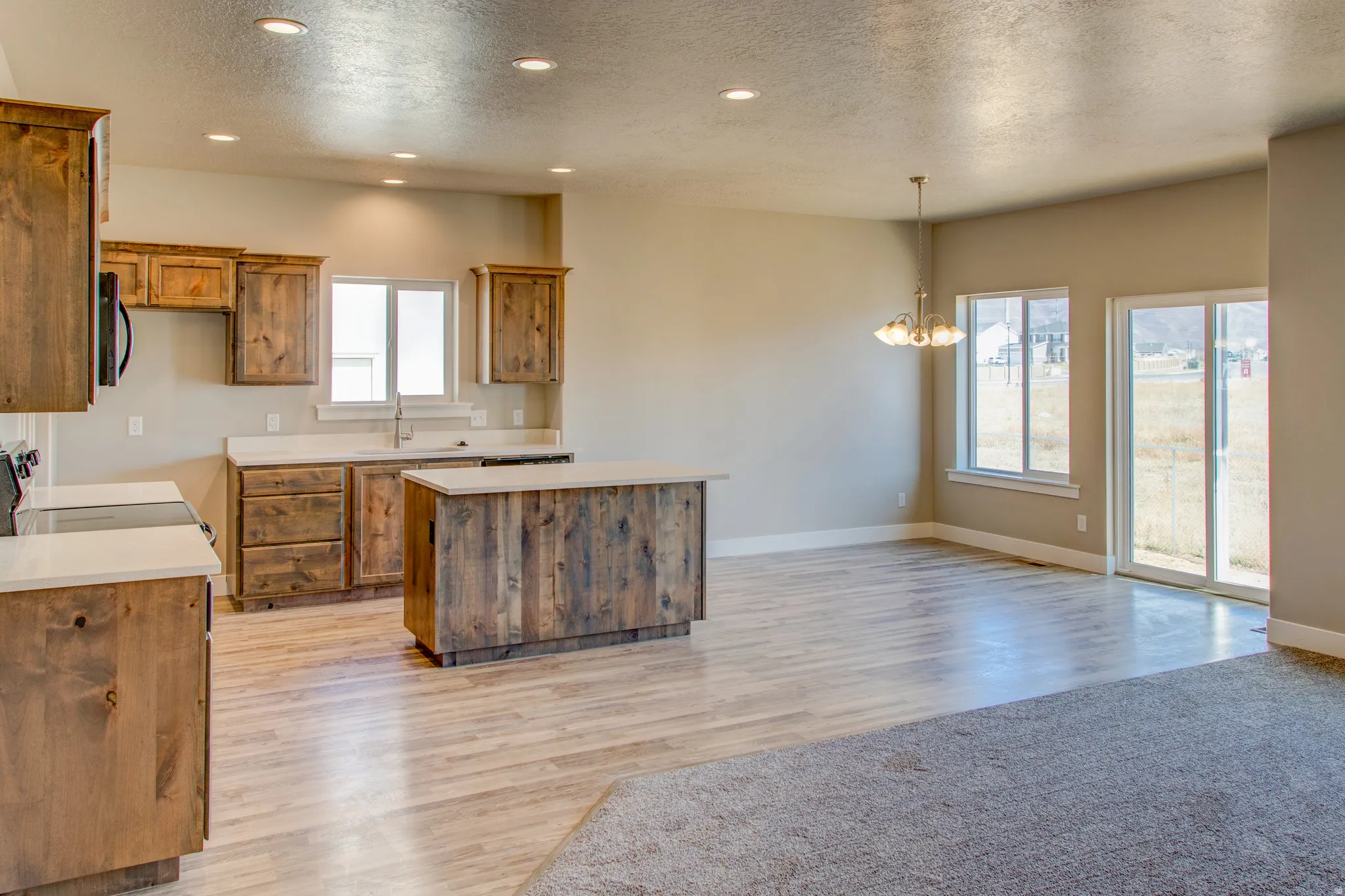 Open-concept living space with recessed lighting, wood-finish flooring, a kitchen island, white countertops, and a sliding glass door