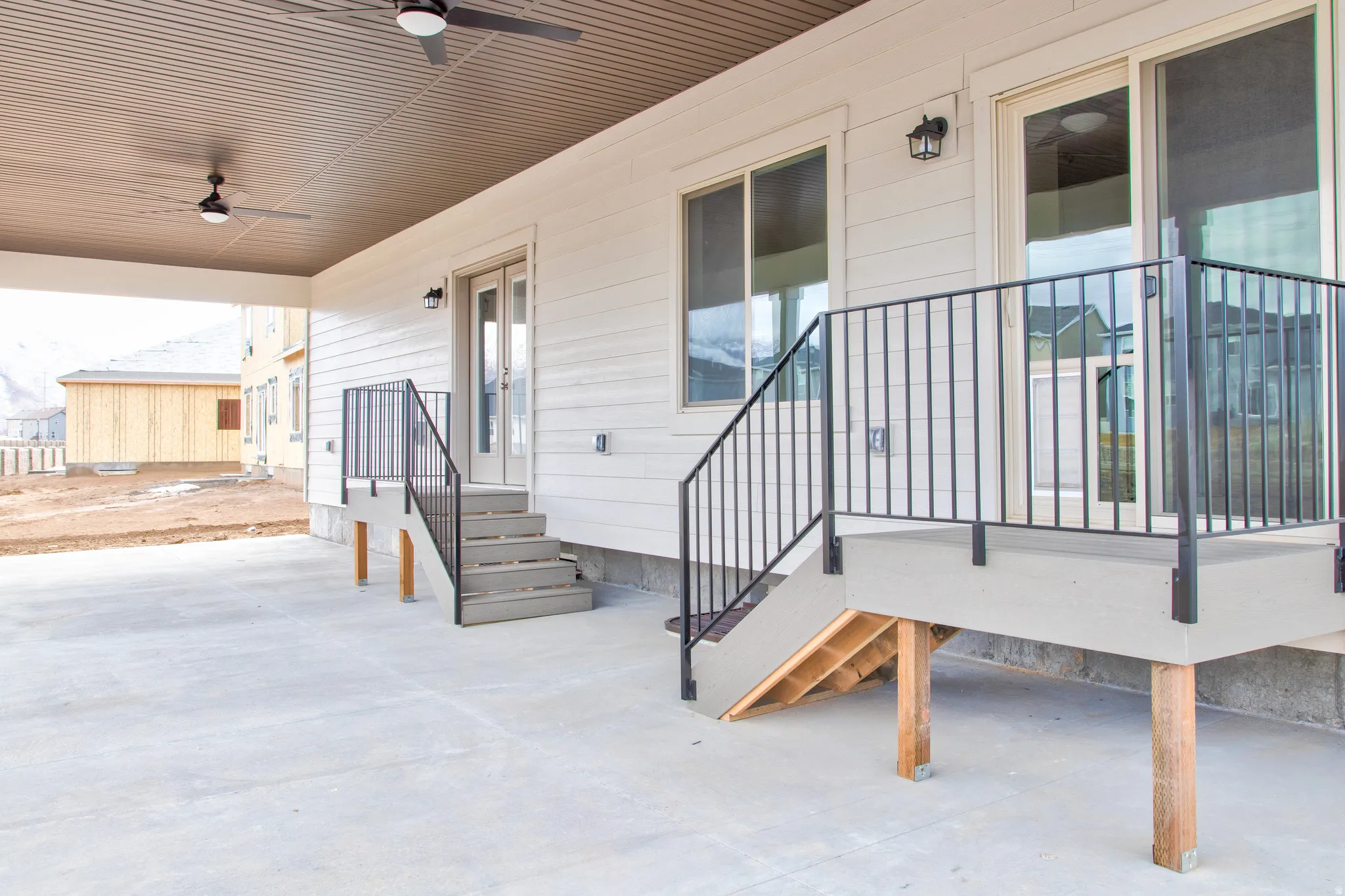 Covered patio with a concrete surface, featuring two ceiling fans, exterior lighting fixtures, and direct access through a glass sliding door