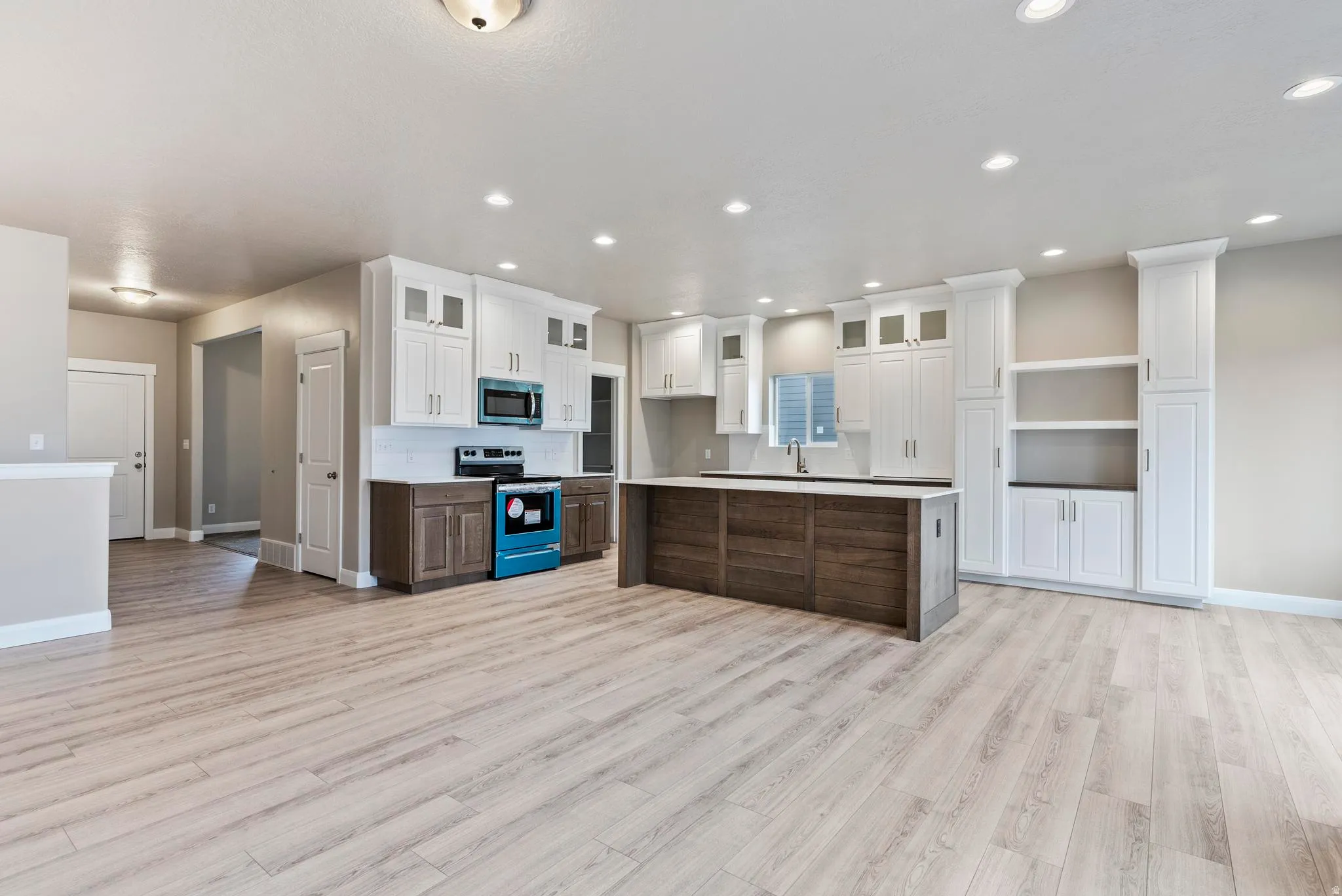 Light wood-finish flooring, white cabinetry, dark wood-finish kitchen island, recessed lighting, and built-in shelving