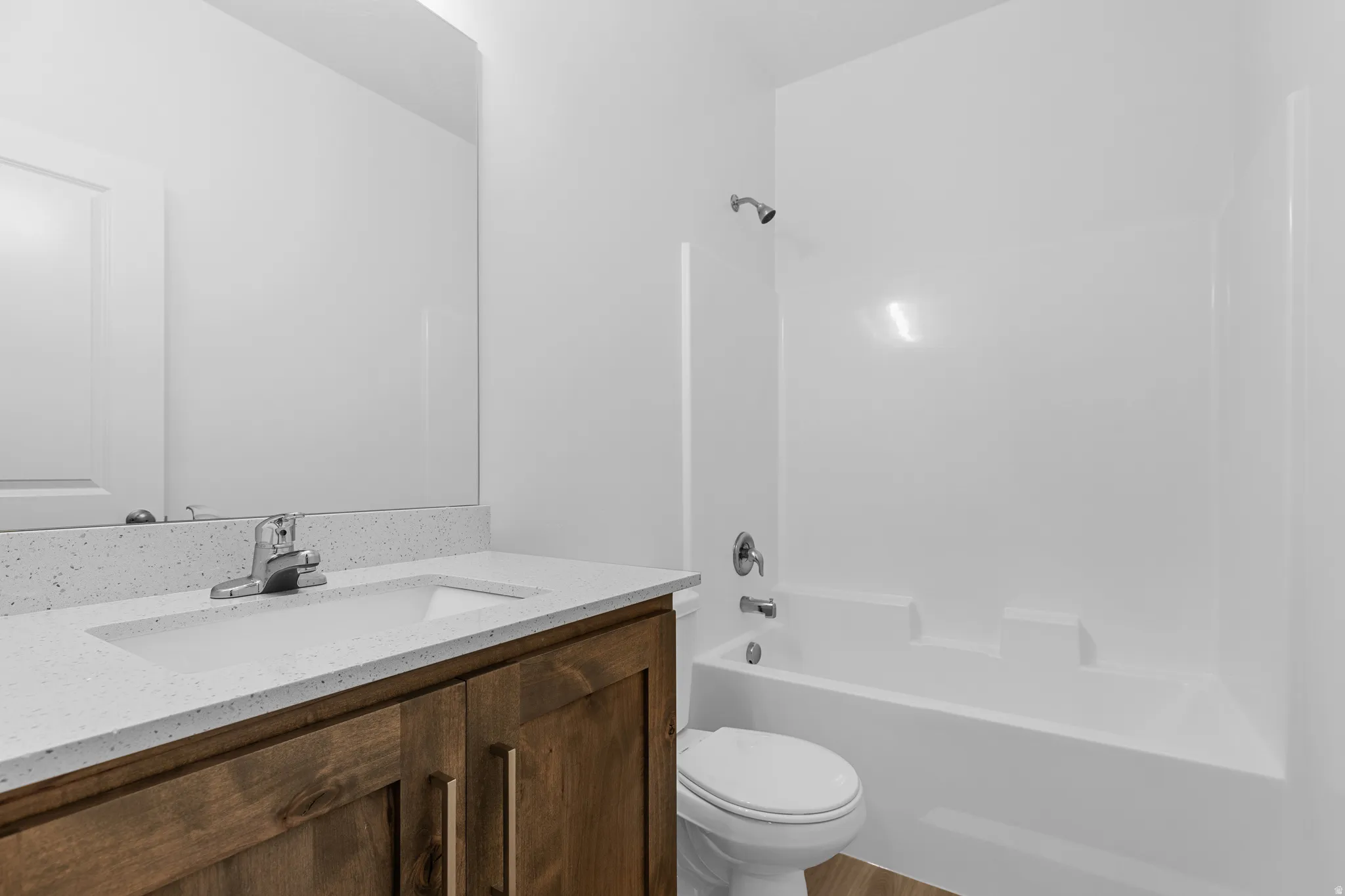 Bathroom featuring a wood-finish vanity, light-toned countertop, integrated sink, chrome faucet, and a white tub with shower