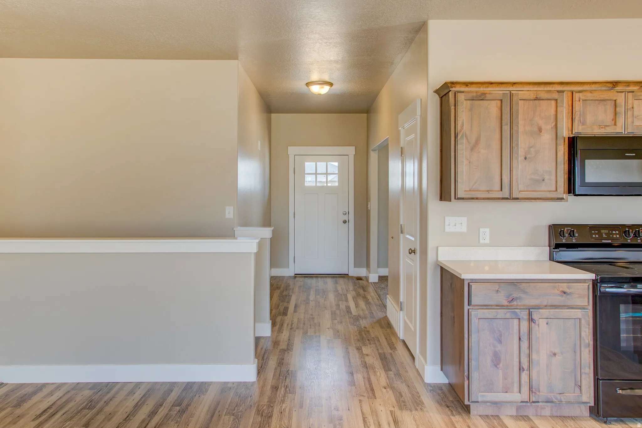 Wood-finish flooring throughout, light neutral wall paint, white trim, and a kitchen featuring wood cabinetry, white countertops, and black appliances