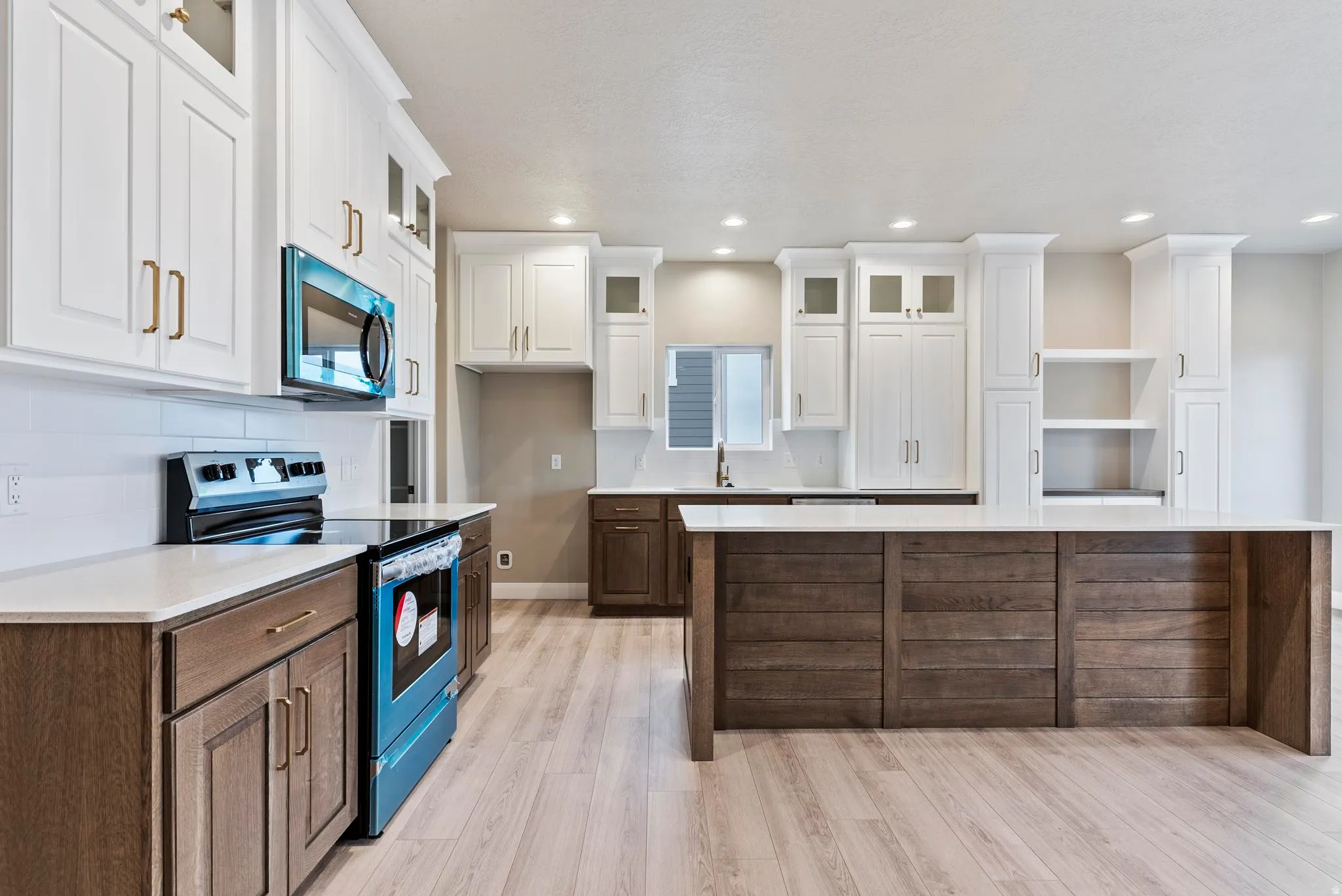 Spacious kitchen featuring white cabinetry, wood-finish flooring, a large center island, and stainless steel appliances