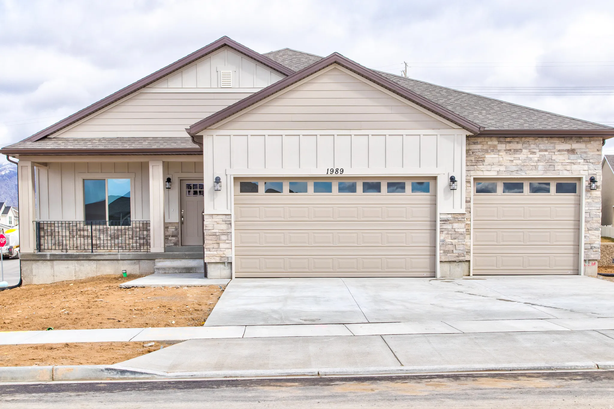 Stone façade accents, dual garage doors with transom windows, covered front porch with railing, vertical and horizontal siding, and concrete driveway