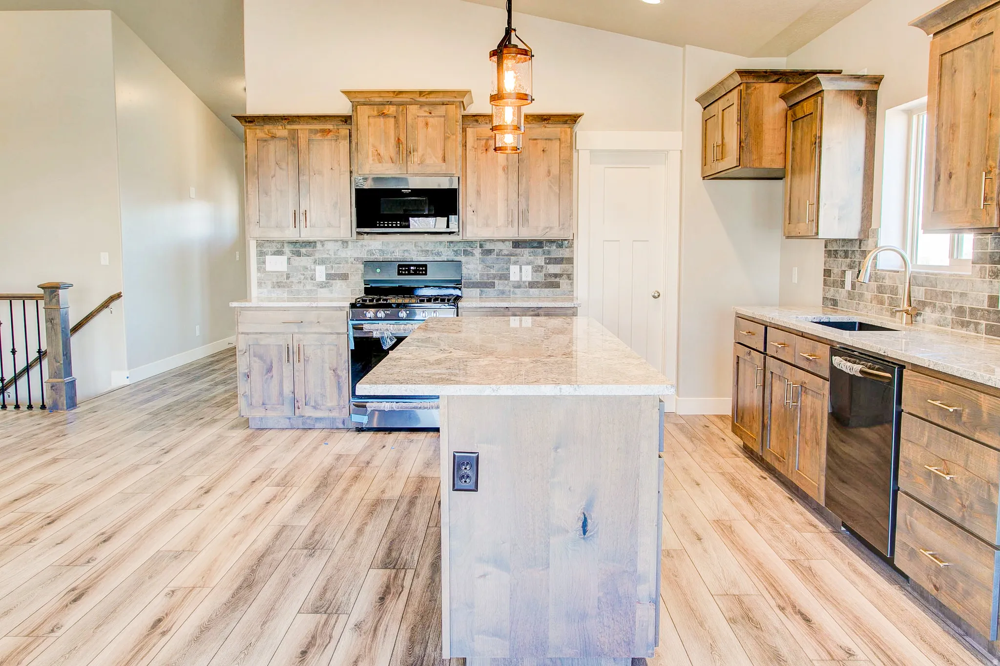 Kitchen featuring wood-finish flooring, granite countertops, tile backsplash, wood cabinetry, and stainless steel appliances
