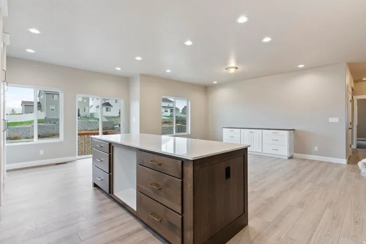 Spacious interior featuring wood-finish flooring, a large kitchen island with integrated storage, built-in white cabinetry with a dark countertop, recessed lighting, and multiple windows