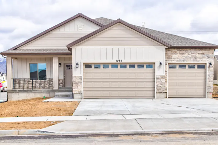 Stone façade accents, dual garage doors with transom windows, covered front porch with railing, vertical and horizontal siding, and concrete driveway