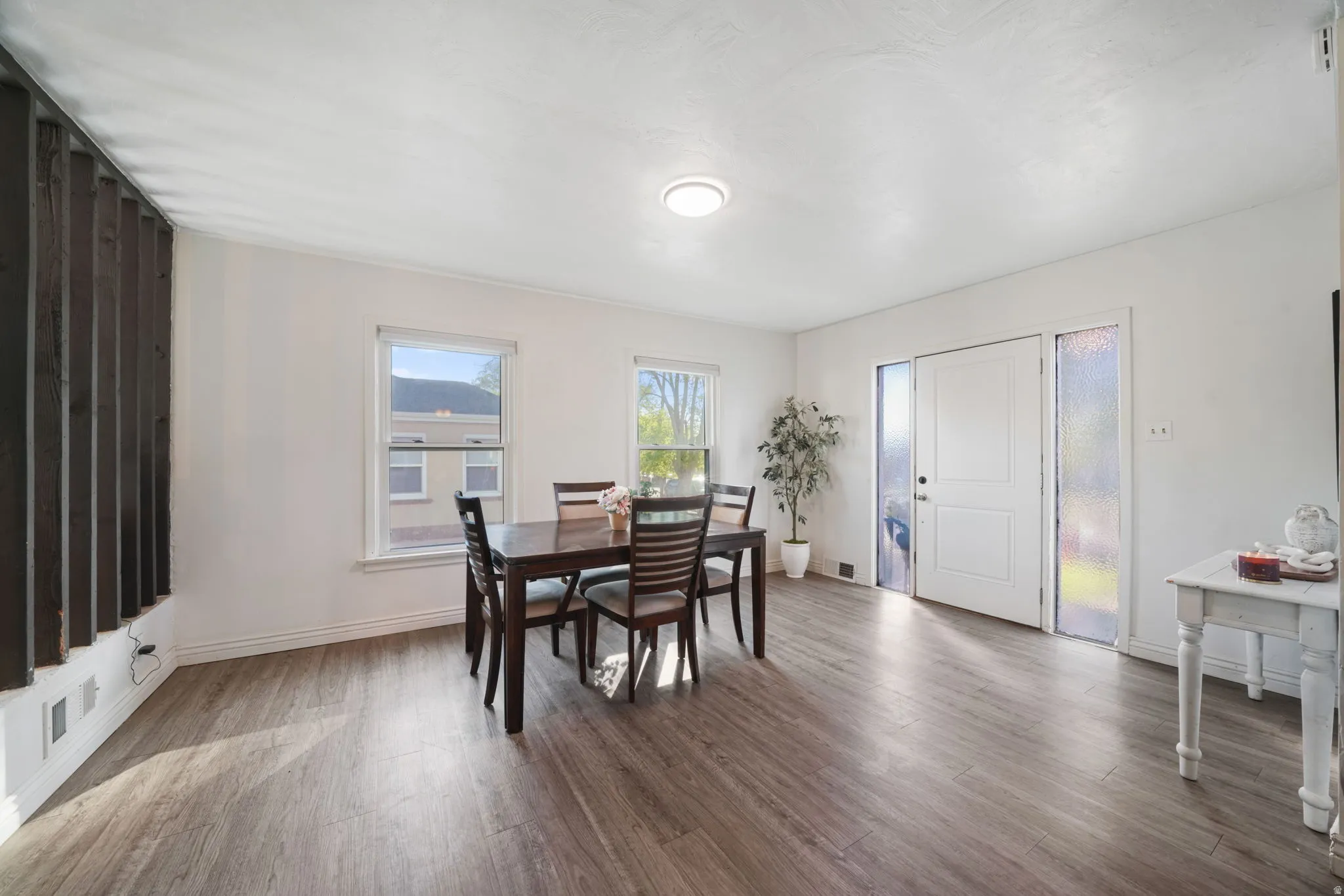 Bright interior with wood-finish flooring, white walls, and a paneled entry door with frosted glass sidelights